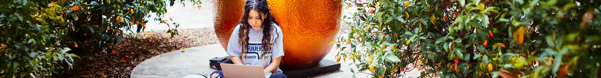 Student on their laptop in front of the citrus statue